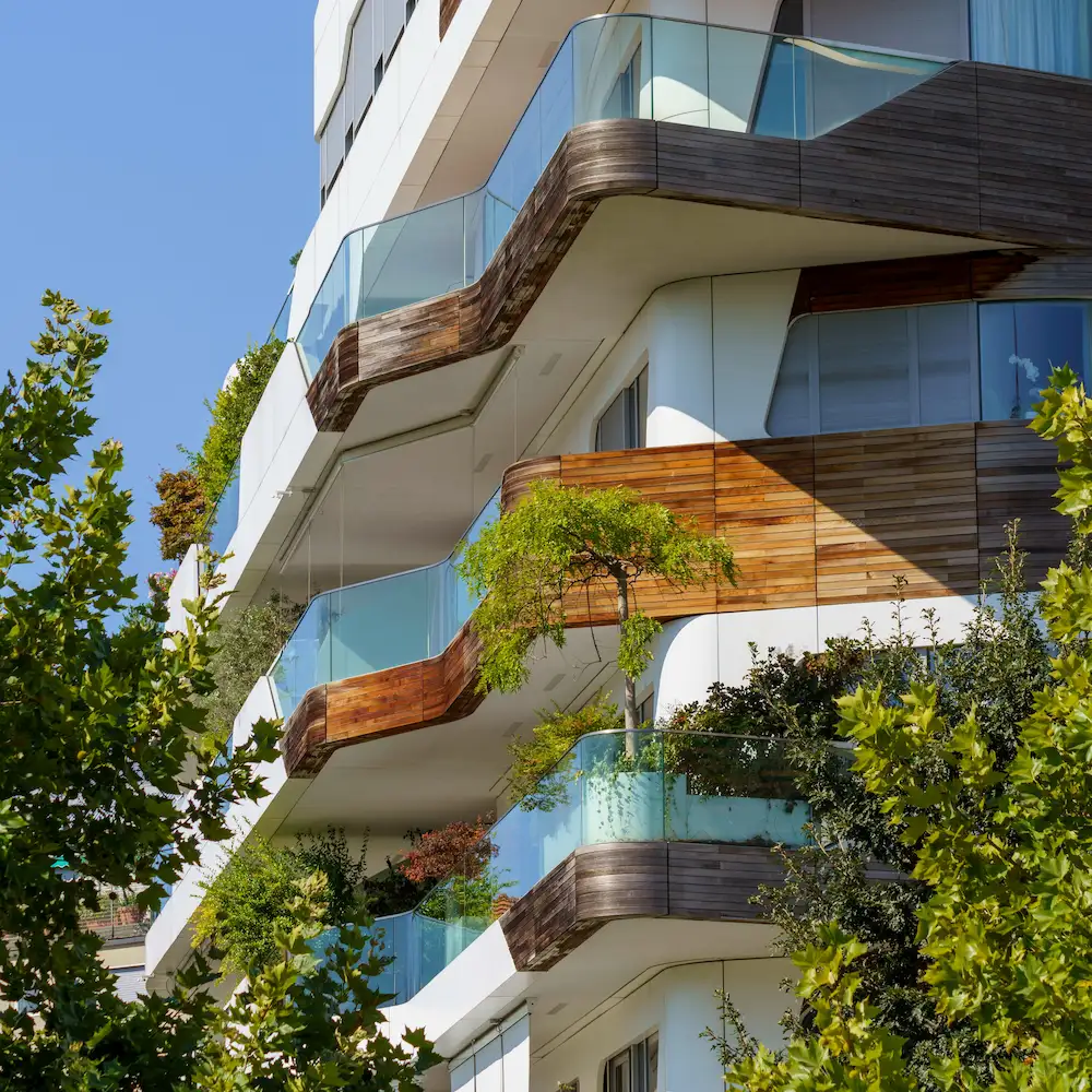 Modernes Mehrfamilienhaus mit großen Balkonen, Pflanzen und geschwungener Fassade.