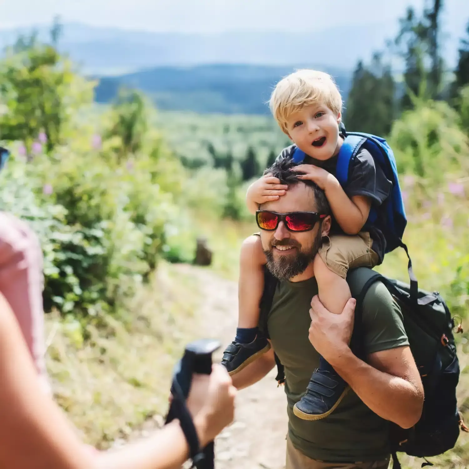 Vater trägt ein kleines Kind auf den Schultern bei einem Ausflug in der Natur.