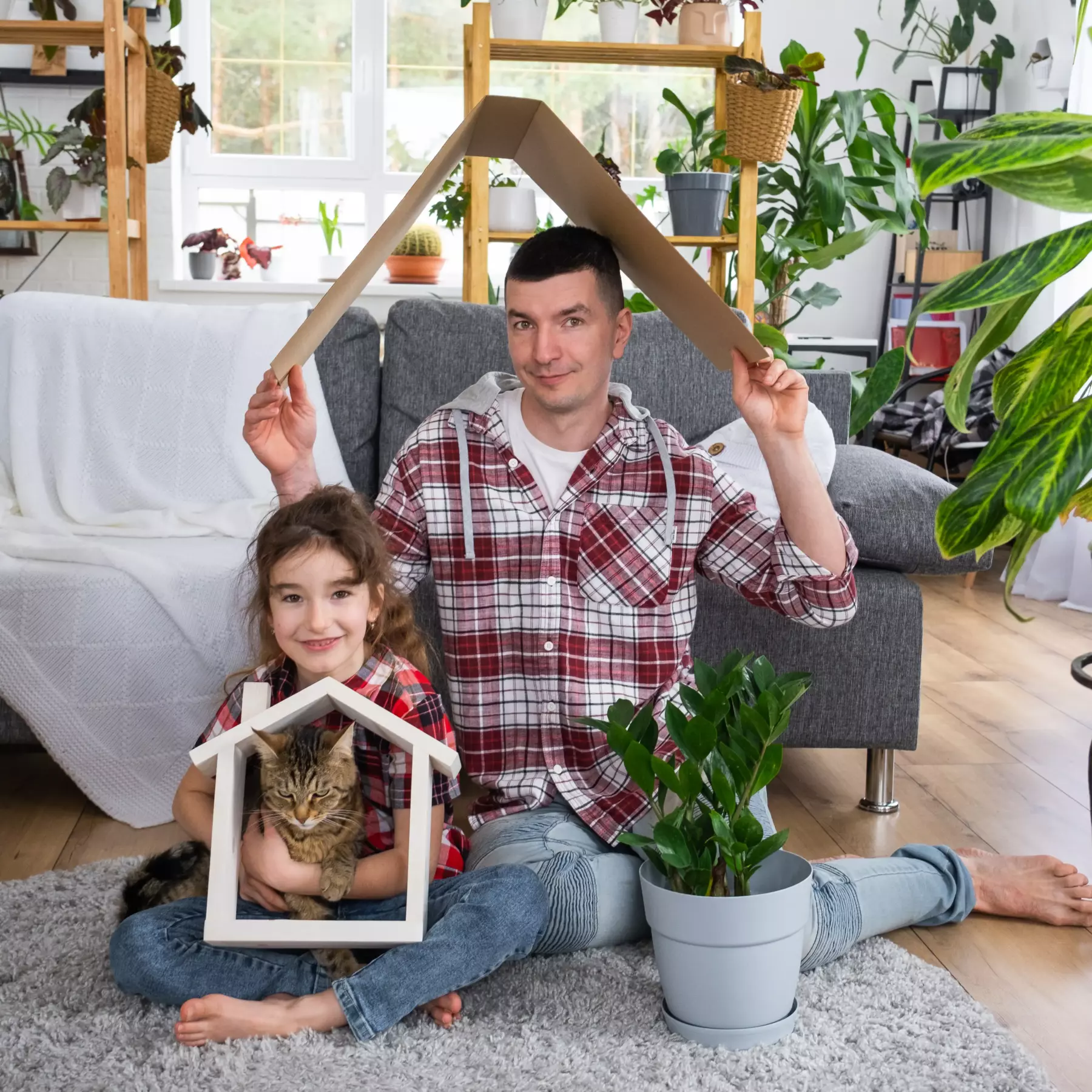 Vater und Tochter sitzen mit einer Katze gemeinsam in einem gemütlichen Wohnraum.