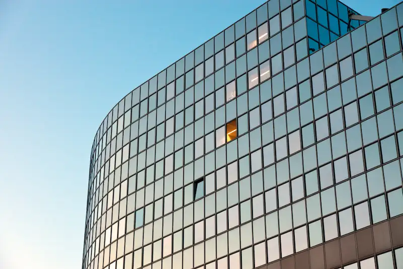 Große Glasfassade eines modernen Bürogebäudes mit einer einzelnen beleuchteten Fensterfläche.