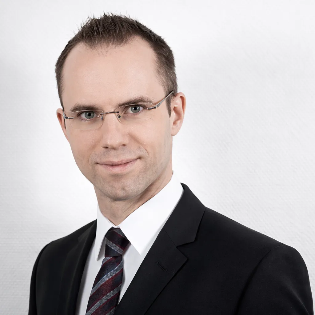 Porträt von Nikolaus Wasmuth im dunklen Anzug vor hellem Hintergrund.