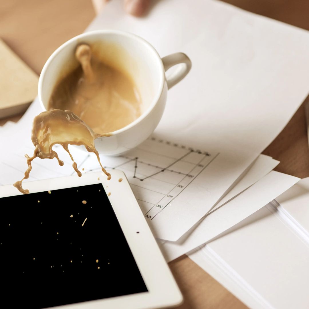 Umgekippte Kaffeetasse liegt neben einem Smartphone und Papieren mit verschüttetem Kaffee.