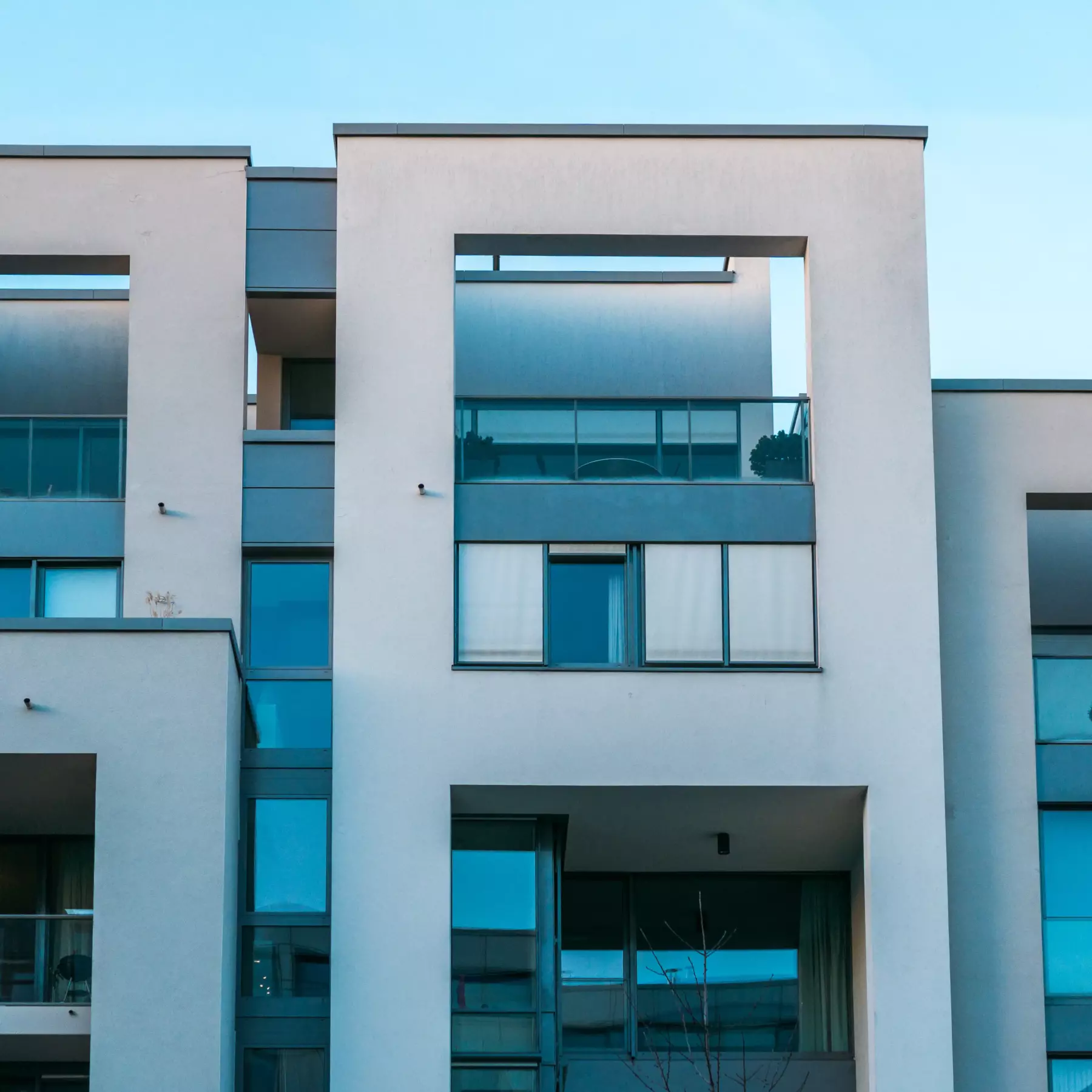 Quadratischer Ausschnitt einer modernen Wohnhausfassade mit Fenstern und klaren Linien.