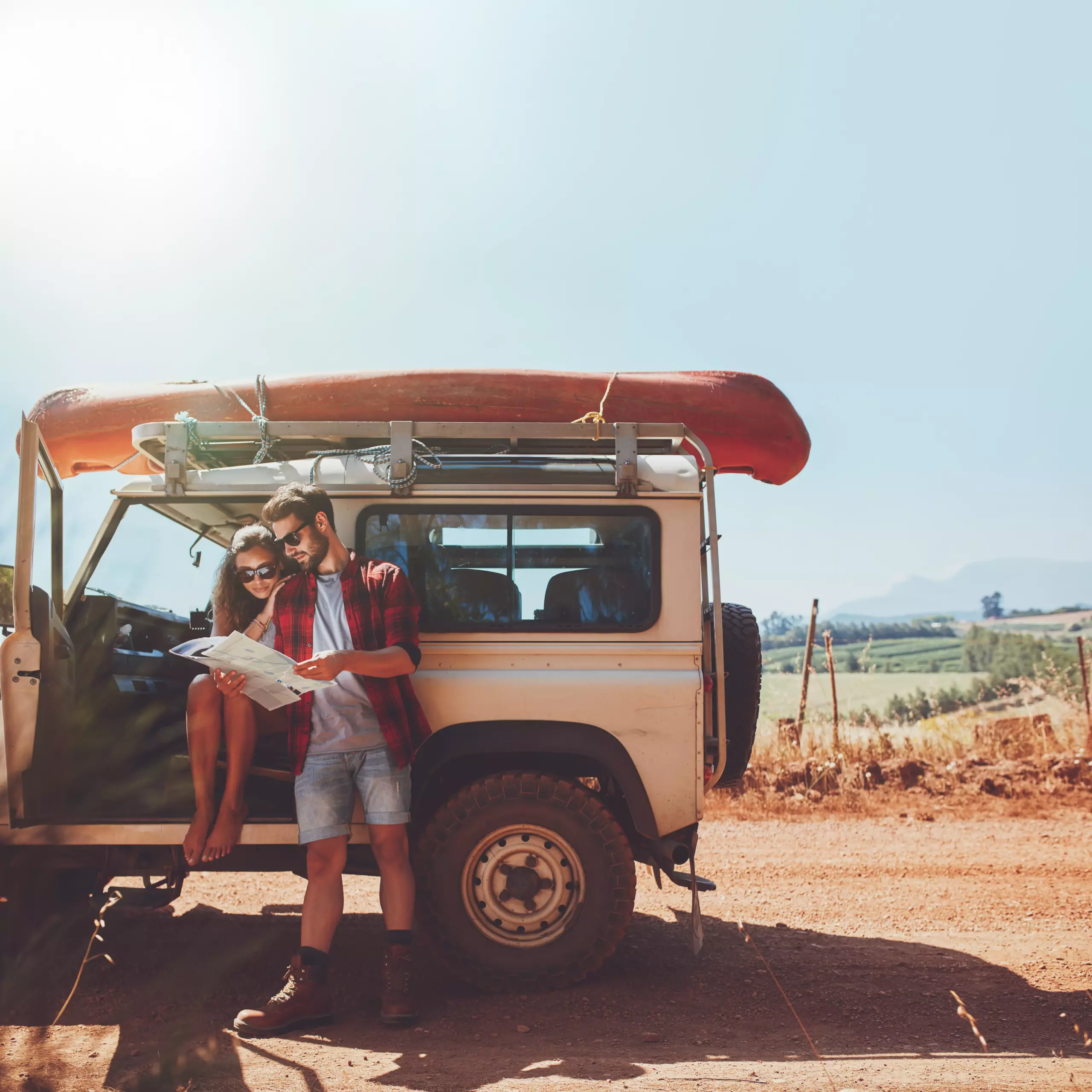 Paar sitzt an einem Geländewagen oder Camper und plant mit Karte einen Roadtrip.