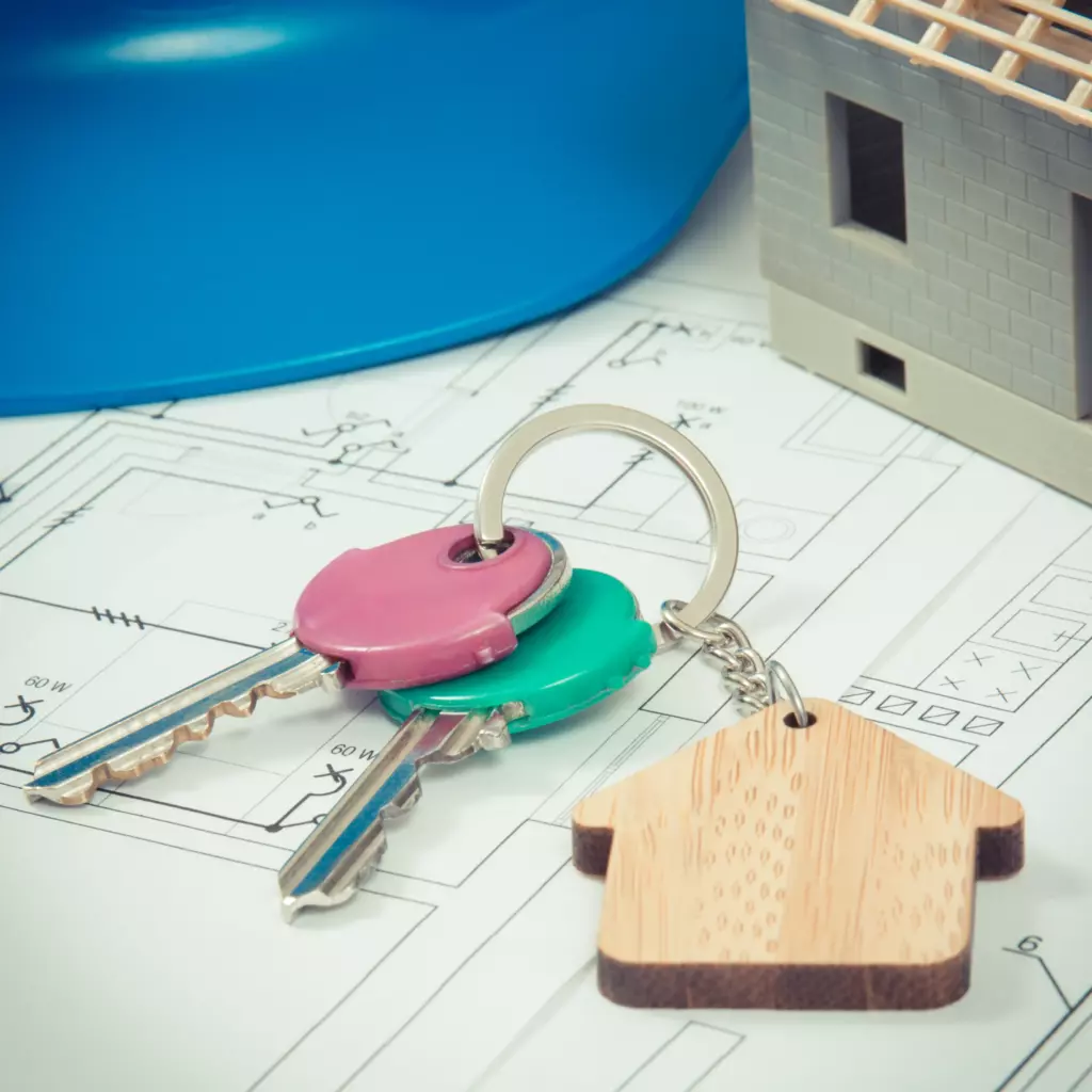 Hausschlüssel und kleines Hausmodell liegen auf einem Bauplan für ein Immobilienprojekt.