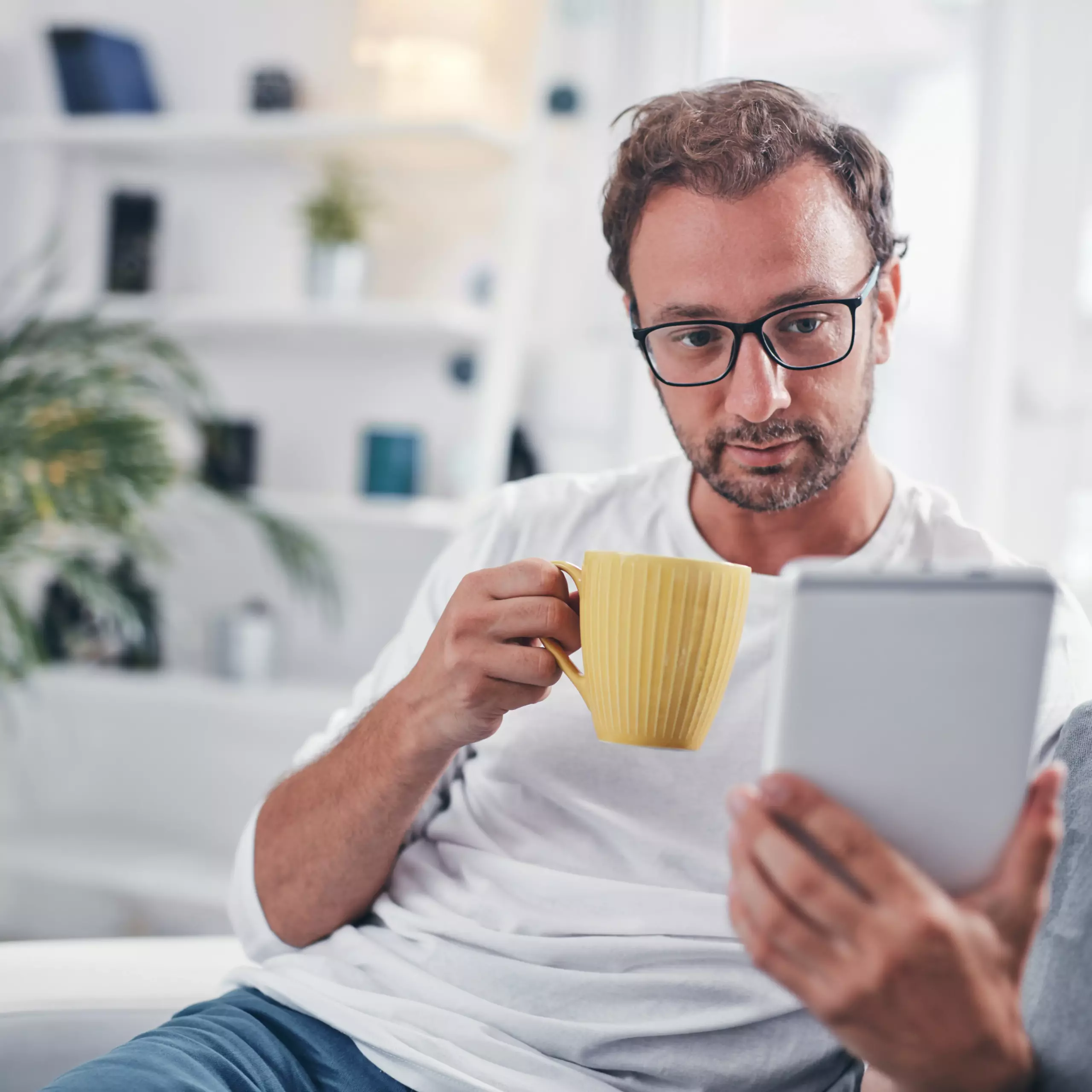 Mann sitzt zu Hause entspannt mit Tablet und Kaffeetasse.