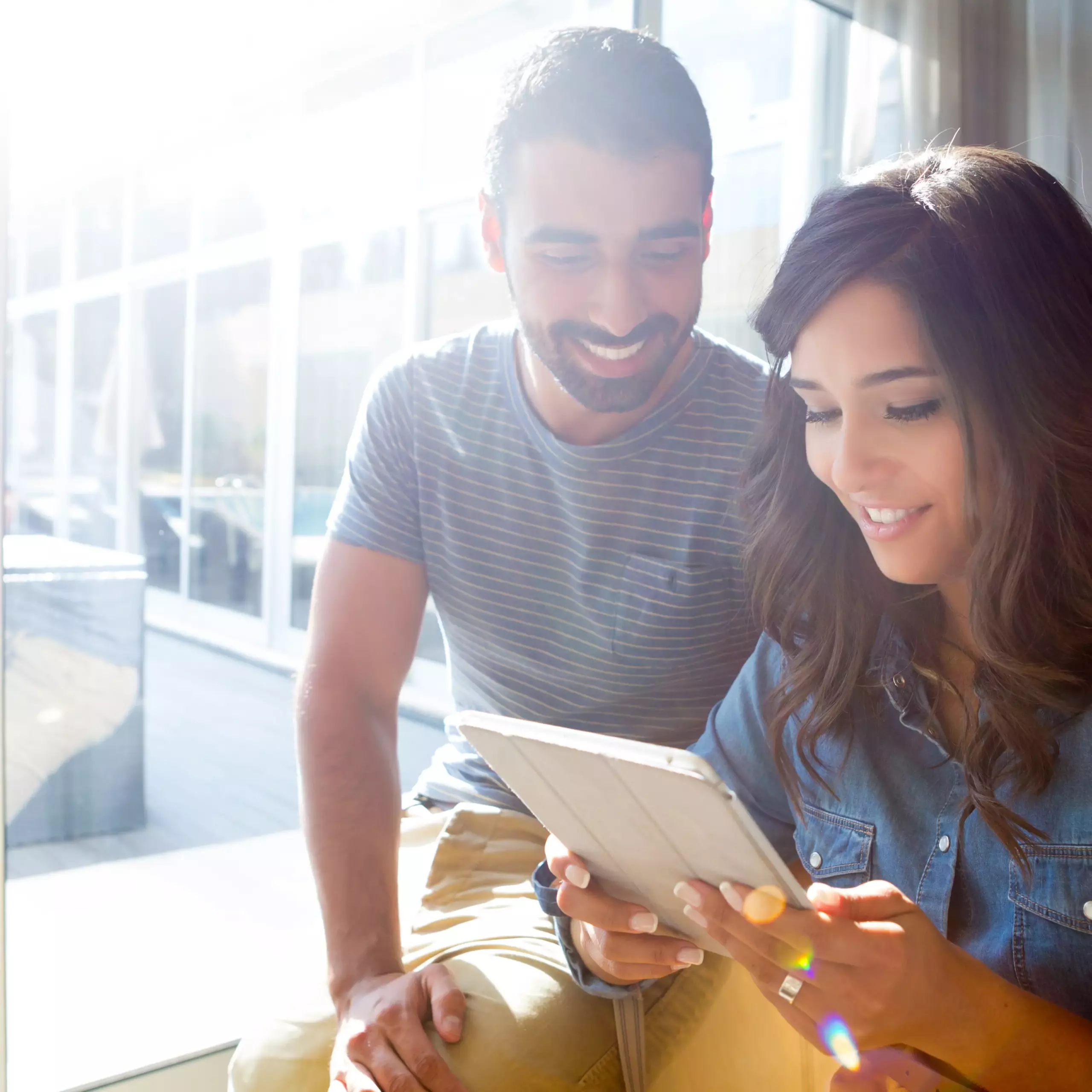 Lächelndes Paar sitzt zusammen und betrachtet Inhalte auf einem Tablet.