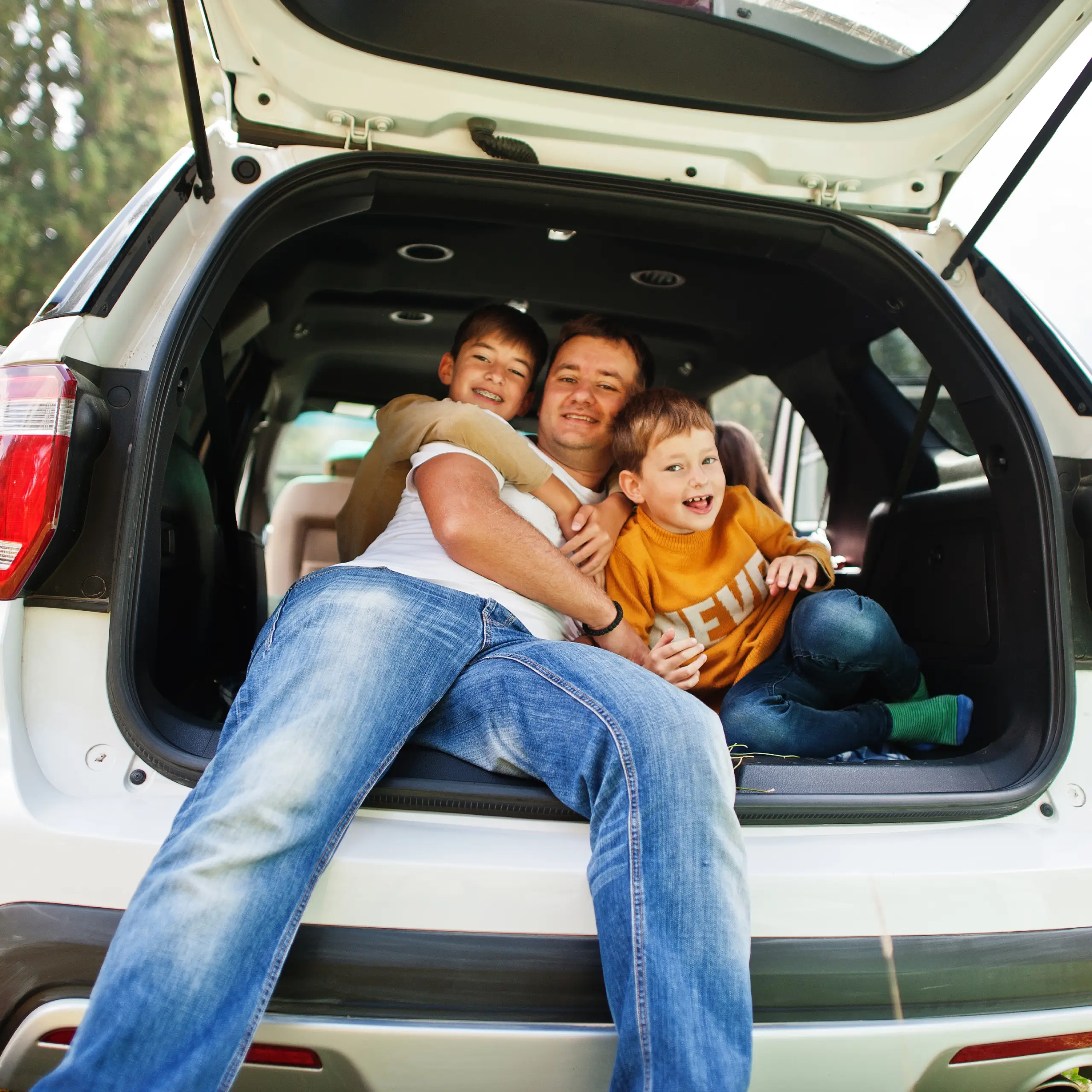 Vater und zwei Kinder verbringen gemeinsam Zeit am geöffneten Kofferraum eines Autos.