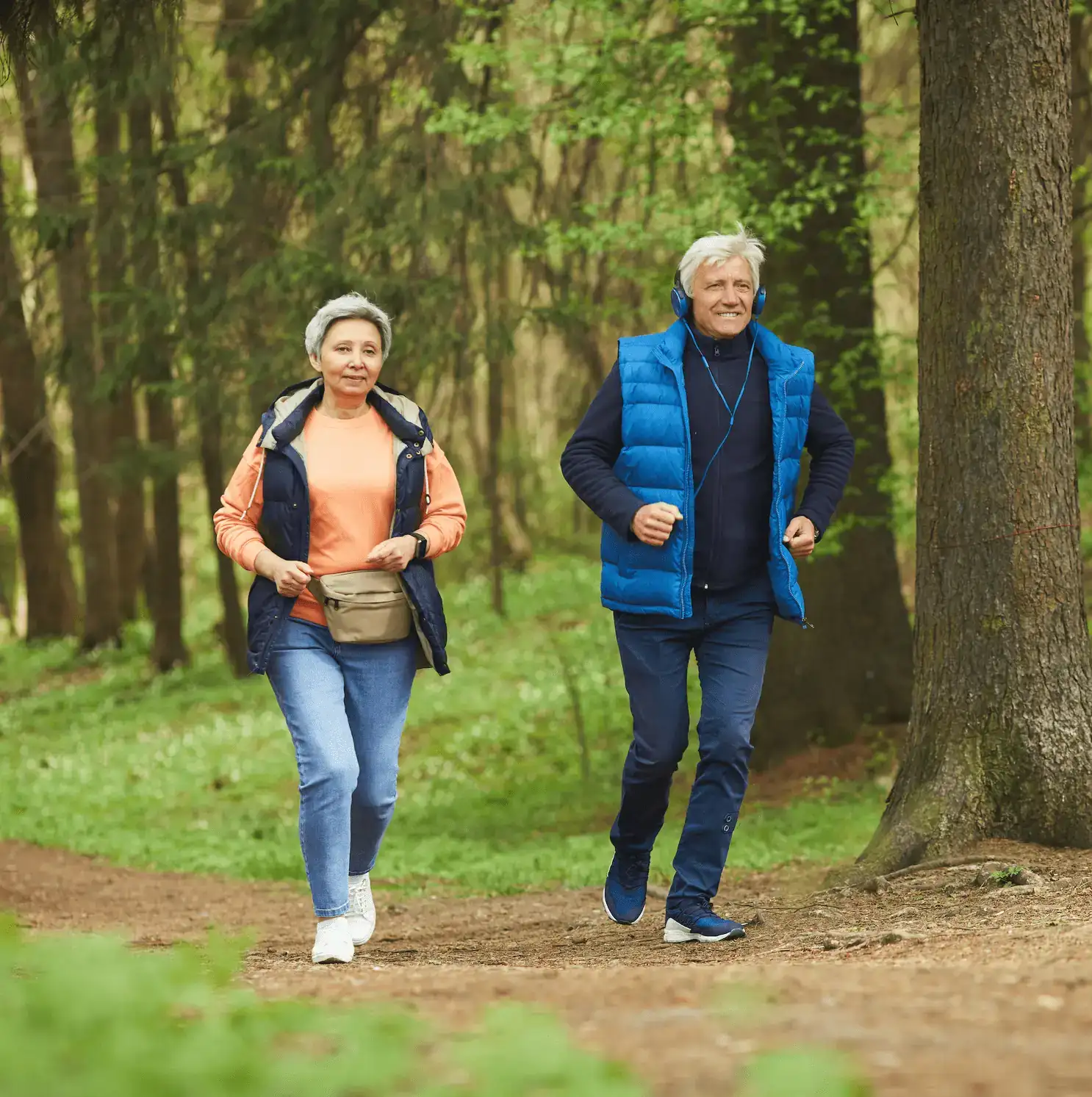 Ältere Frau und älterer Mann sind sportlich auf einem Waldweg unterwegs.