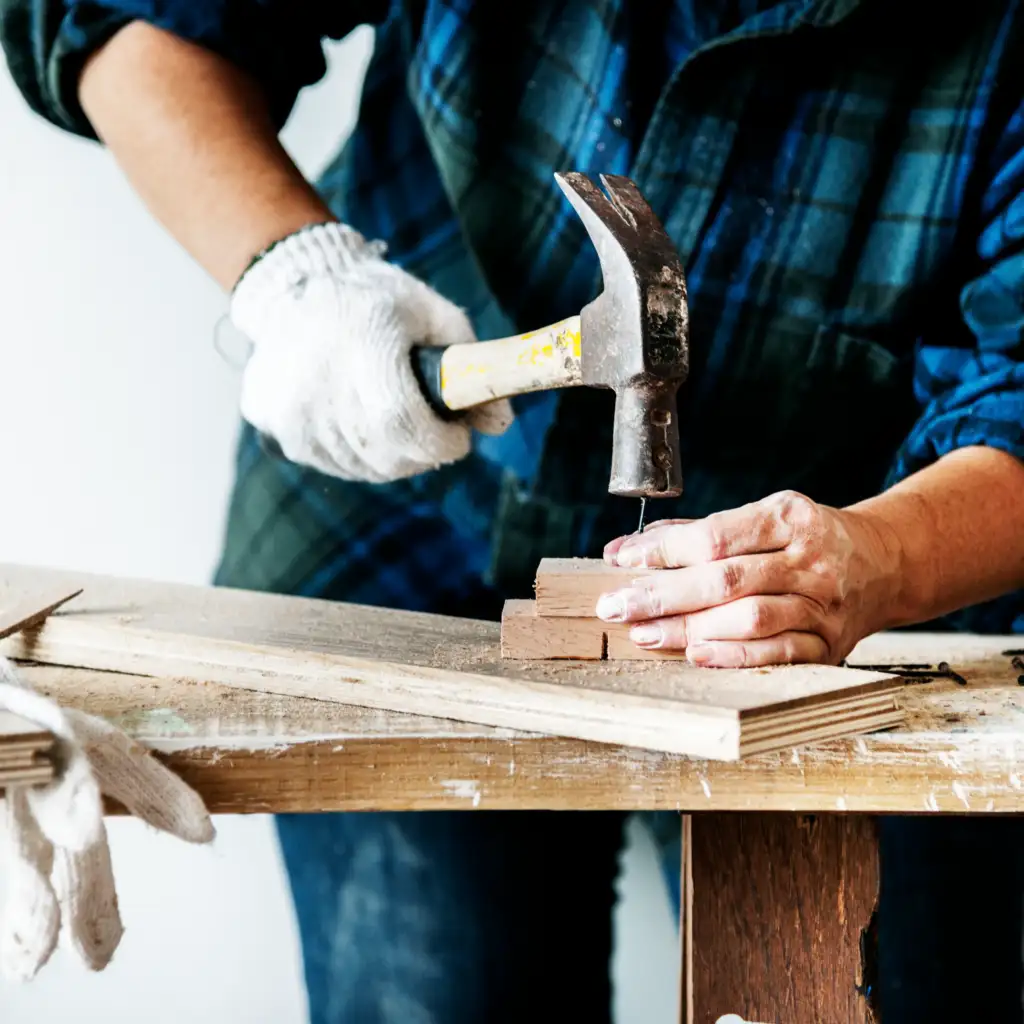 Handwerker arbeitet mit einem Hammer an einem Holzstück in einer Werkstatt.