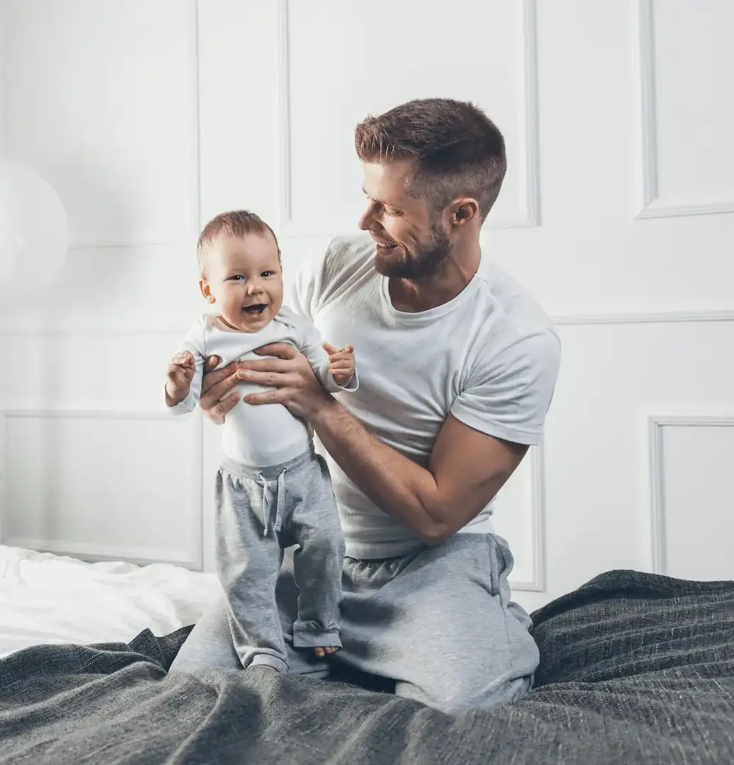 Vater sitzt mit seinem Baby auf einem Bett und verbringt Zeit mit ihm.