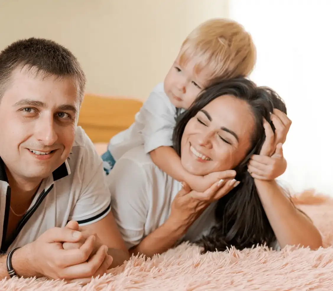 Eltern und Kind liegen eng zusammen auf einem Bett und lachen miteinander.