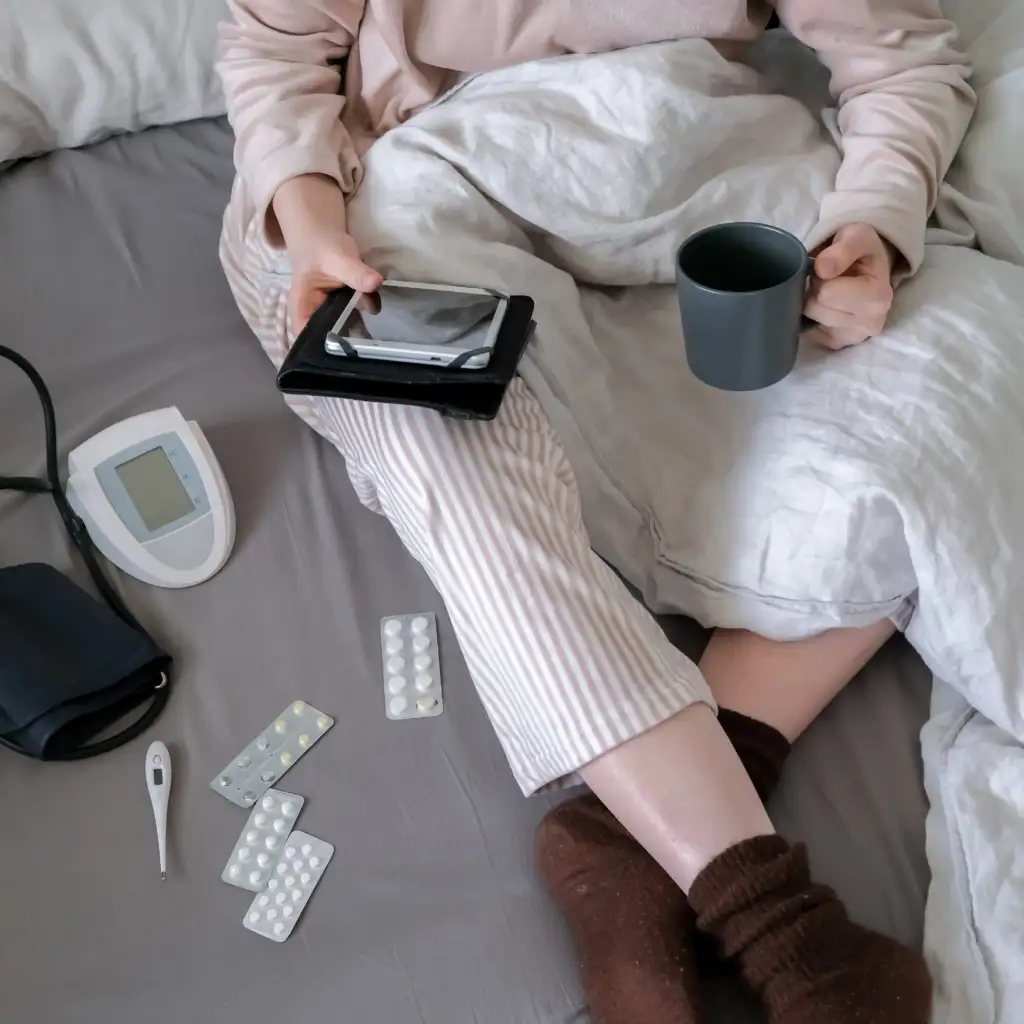 Frau sitzt entspannt im Bett; neben ihr liegen Medikamente und ein Smartphone.